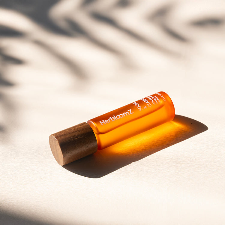 HerbloomZ Focus & Clarity essential oil lying in sunlight — natural wood cap and amber glass bottle on warm neutral background. - HerbloomZ