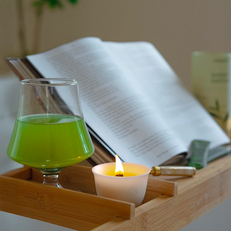 Glass of probiotic matcha on a wooden tray with a lit candle and an open book in the background.