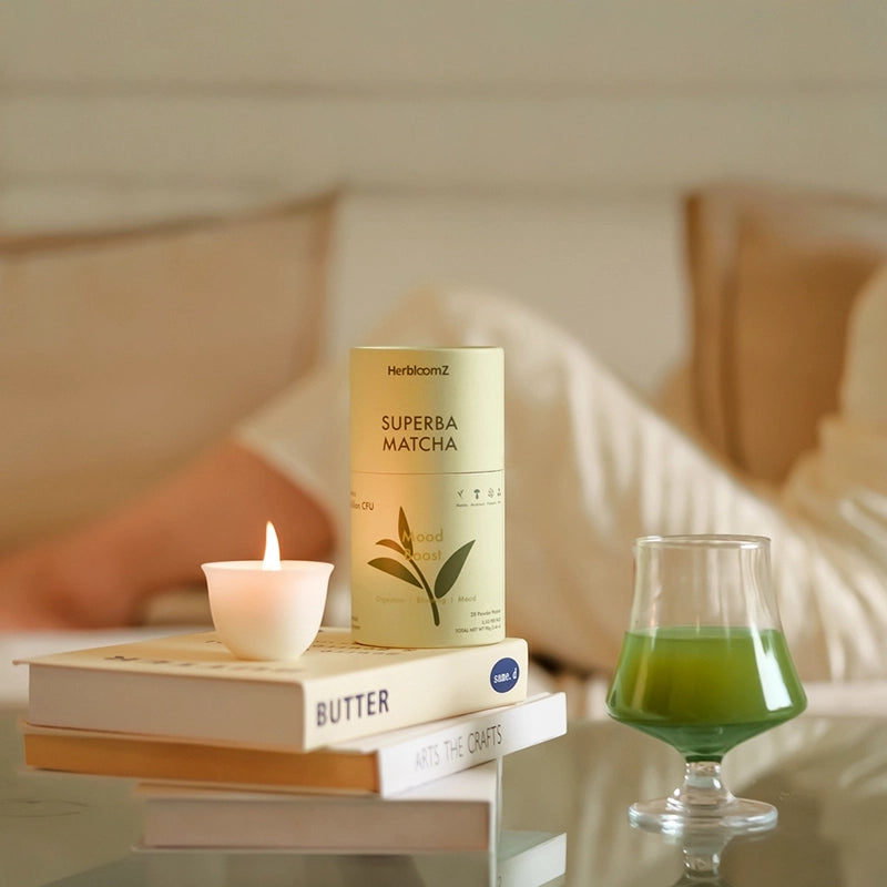 A cozy evening ritual with HerbloomZ SUPERBA MATCHA, a lit Bamboo Zen candle, and a glass of calming probiotic matcha resting on books