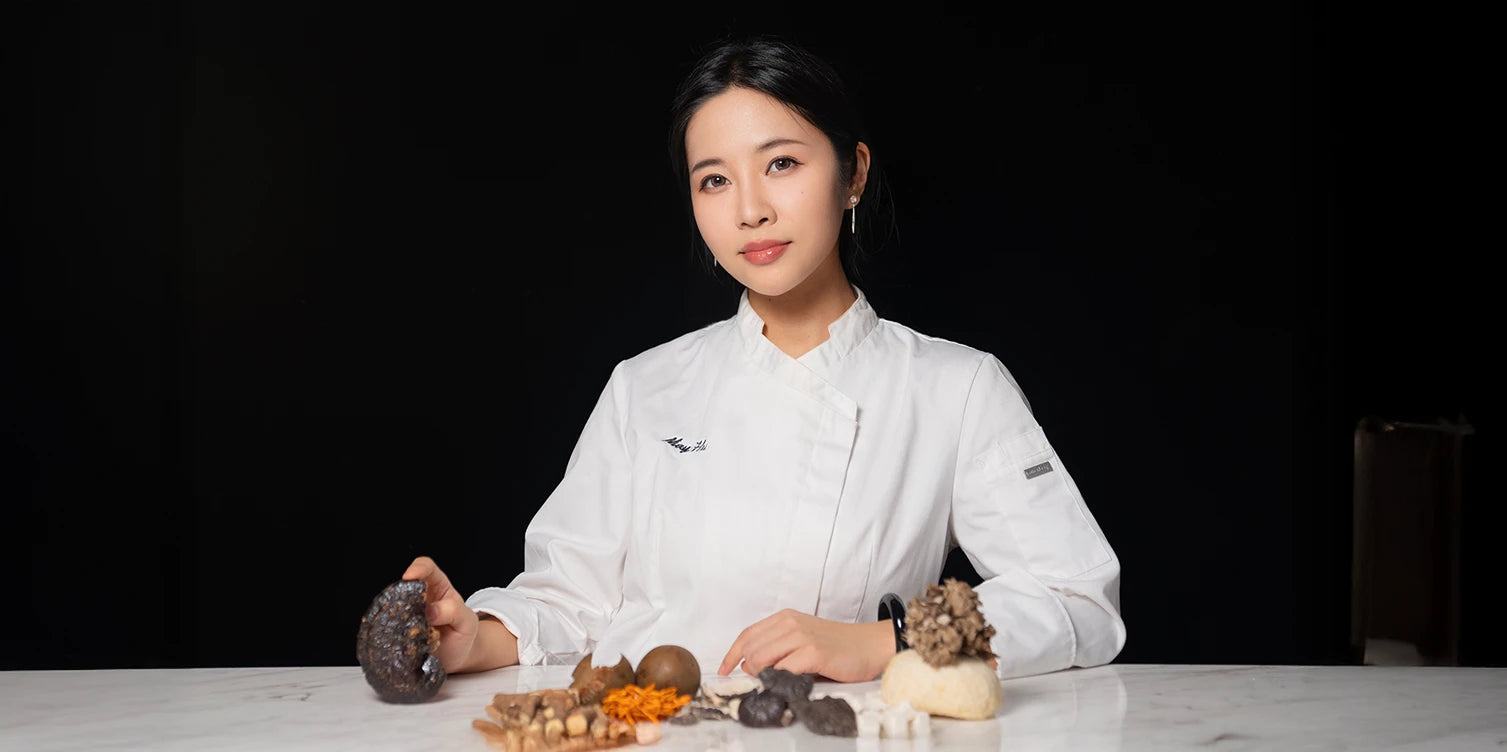 HerbloomZ founder in chef’s coat with TCM herbs and functional mushrooms — blending Traditional Chinese Medicine and modern nutrition for stress relief and gut health