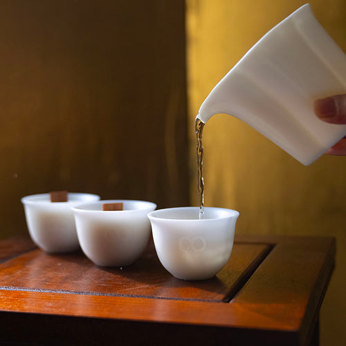 Hand pouring hot water into HerbloomZ Dehua porcelain cups used as candle vessels or tea cups, creating a serene ritual scene - HerbloomZ