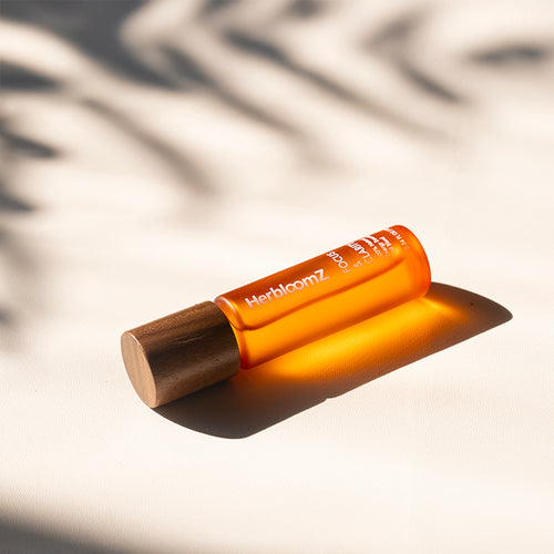 HerbloomZ Focus & Clarity essential oil lying in sunlight — natural wood cap and amber glass bottle on warm neutral background. - HerbloomZ