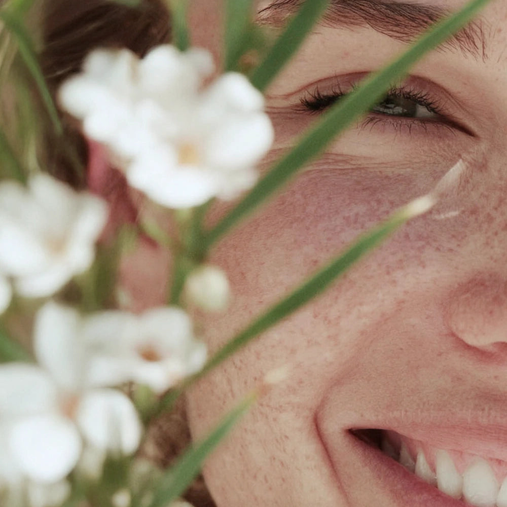 Close-up smile behind white flowers in soft light — HerbloomZ SUPERBA MATCHA lifestyle visual for probiotic, gut-friendly matcha