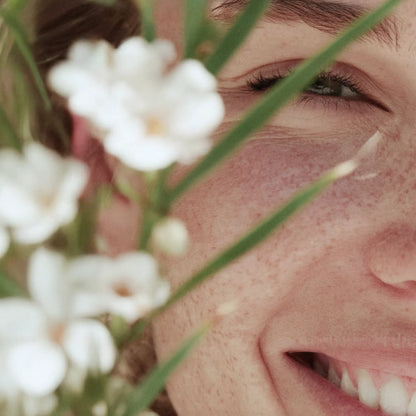 Close-up smile behind white flowers in soft light — HerbloomZ SUPERBA MATCHA lifestyle visual for probiotic, gut-friendly matcha