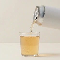 Tea being poured from a can into a glass on a light background
