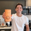Man holding a can of  HERBLOOMZ SUPERBA coffee in a kitchen